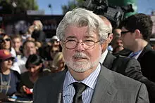 Homme avec une barbe et des cheveux blancs qui porte des petites lunettes rondes.